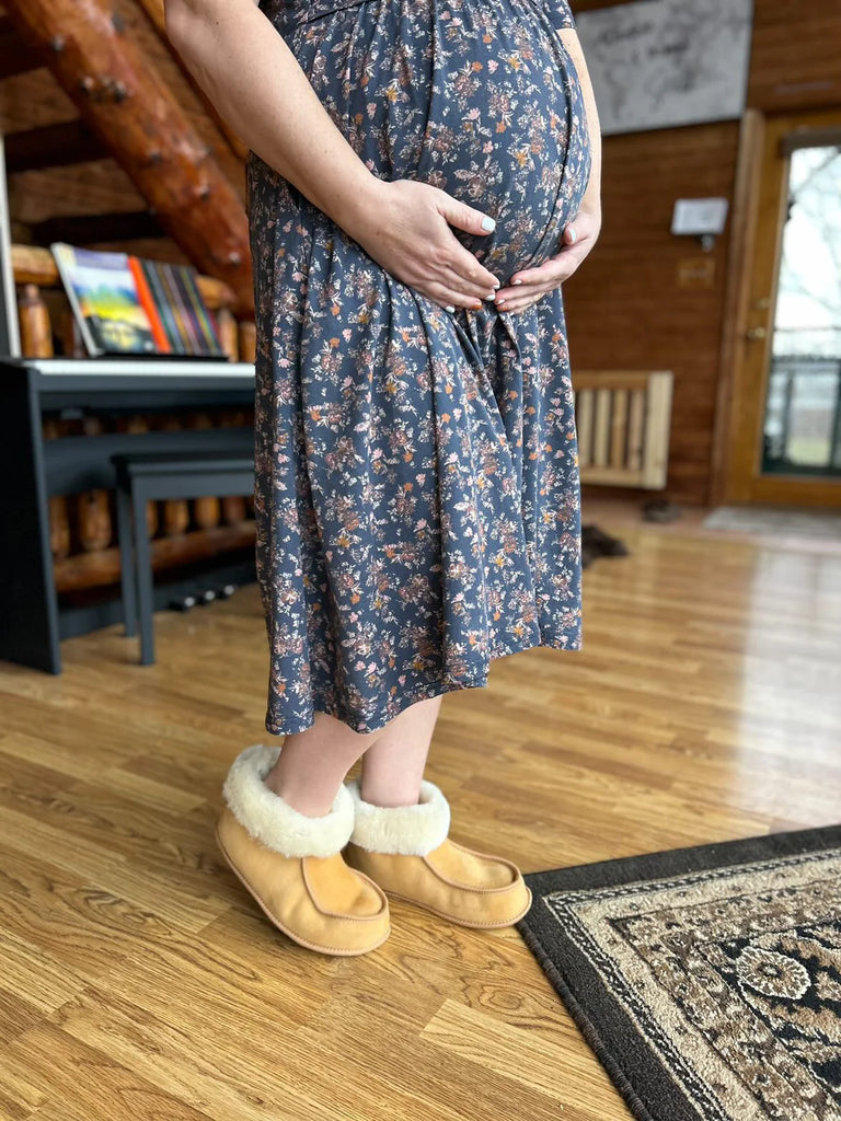 Pregnant person wearing a floral dress and terra slipper sheepskin minimalist footwear tan